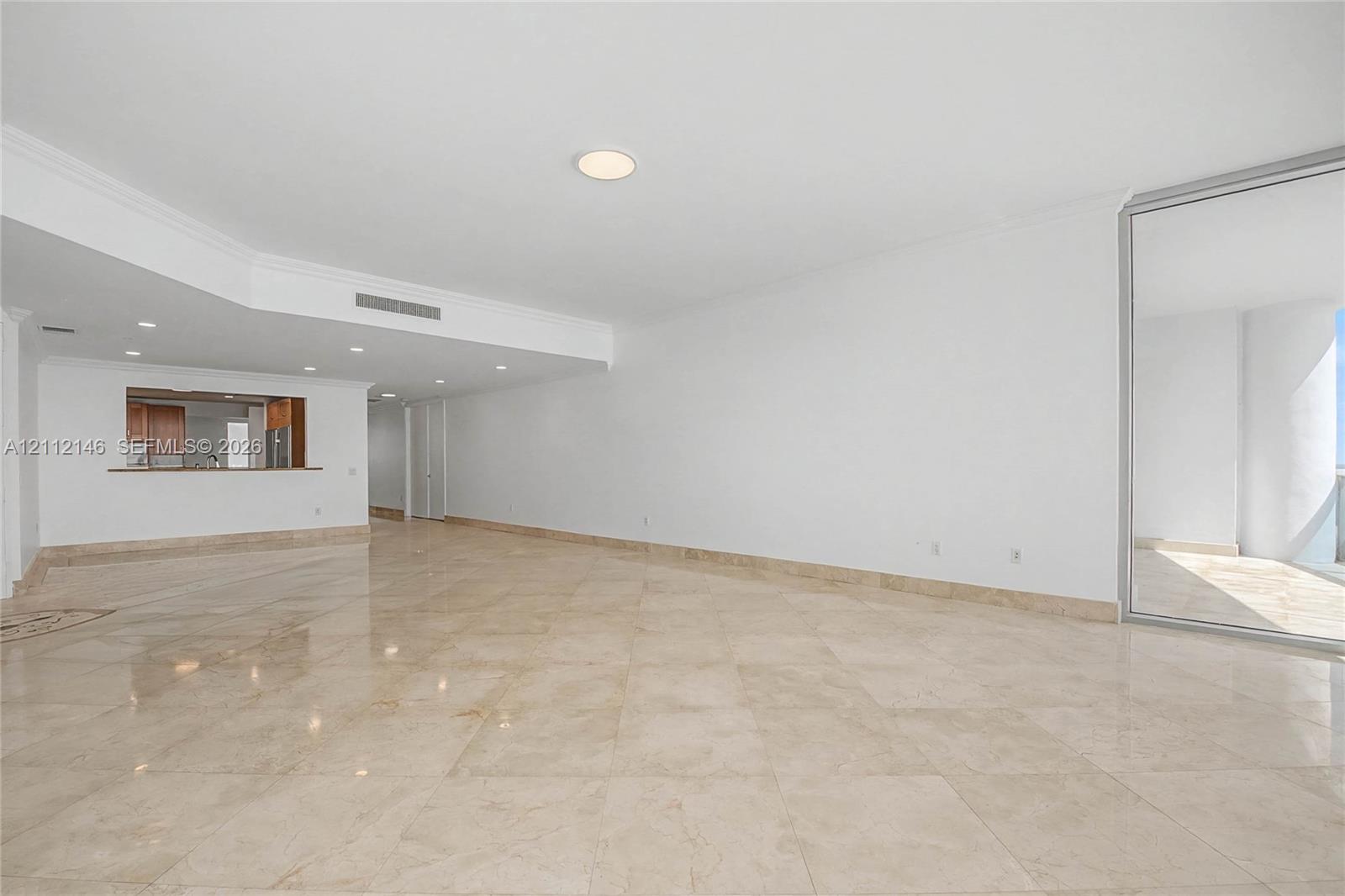 Open-concept interior featuring large-format stone tile flooring, recessed ceiling lighting, crown molding, a service pass-through window, and floor-to-ceiling glass paneling