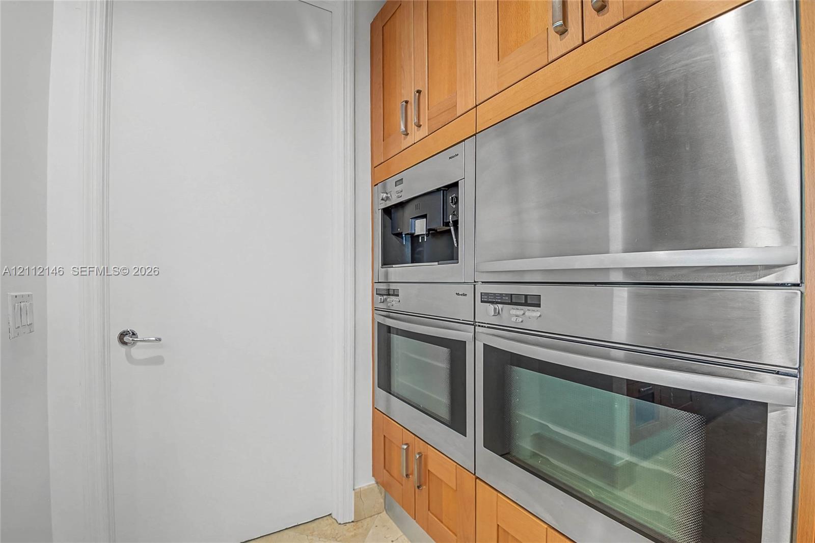 Built-in stainless steel appliances including a coffee system and dual ovens, integrated into custom wood-finish cabinetry with metallic hardware