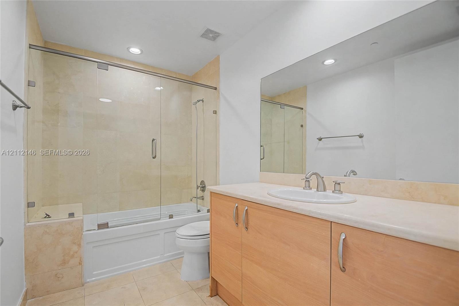 Wood-finish vanity with light-toned countertop, undermount sink, frameless glass shower enclosure, and neutral tile surround