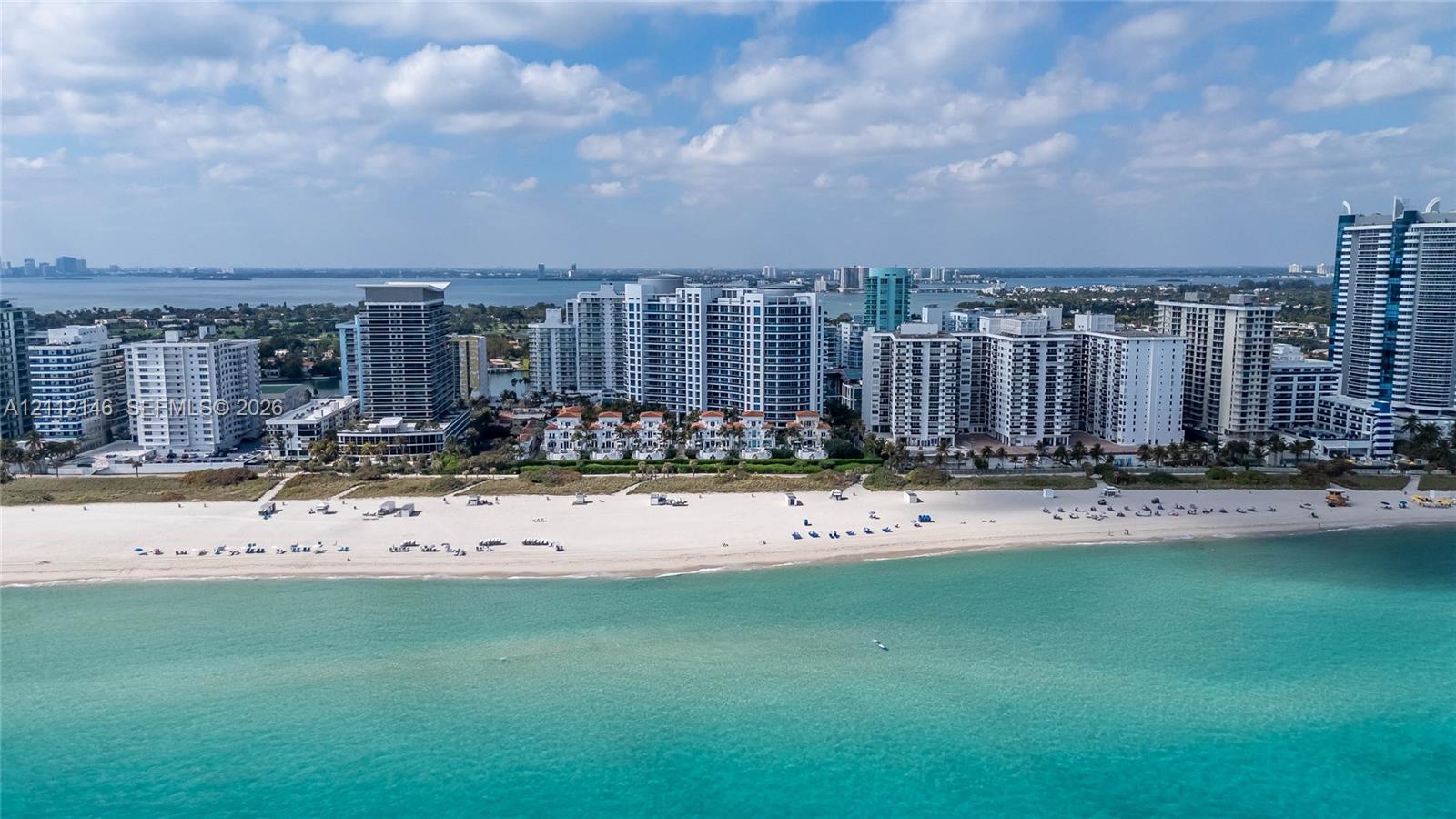 Aerial perspective of coastal property featuring direct oceanfront access, white sand beach, and dense urban skyline
