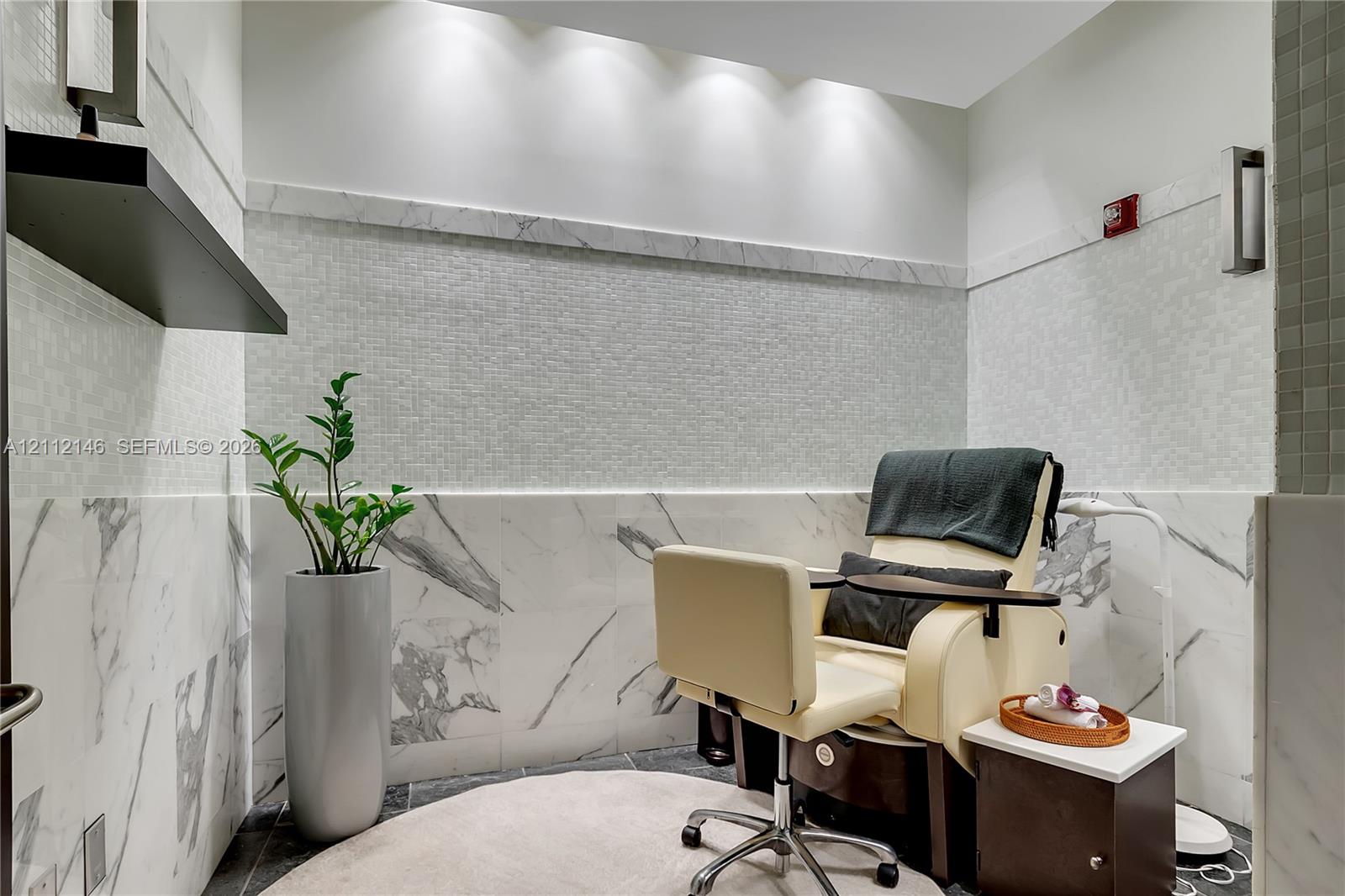 Polished stone wall tile, mosaic tile accent wall, recessed ceiling lighting, and built-in floating shelf