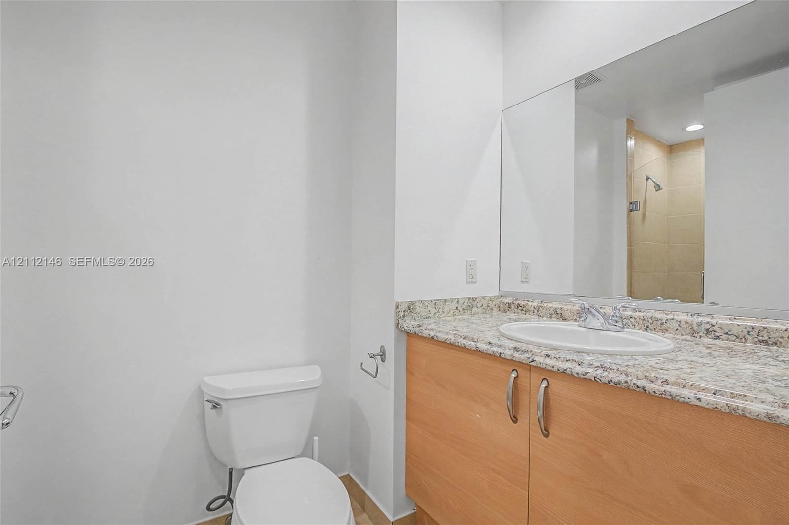 Bathroom featuring a vanity with light-tone wood-finish cabinetry, a neutral-toned stone countertop, an integrated oval sink, and a large-format vanity mirror