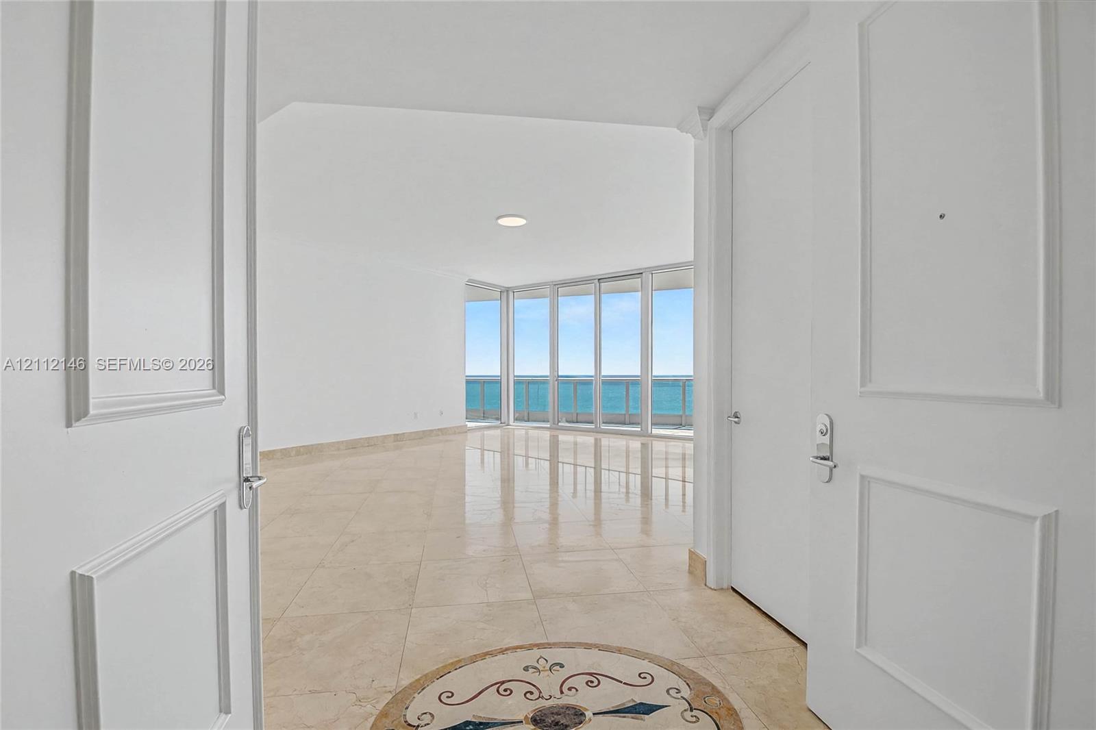 Interior entry featuring dual-panel doors, large-format tile flooring with a circular stone inlay medallion, and floor-to-ceiling glass windows offering water exposure