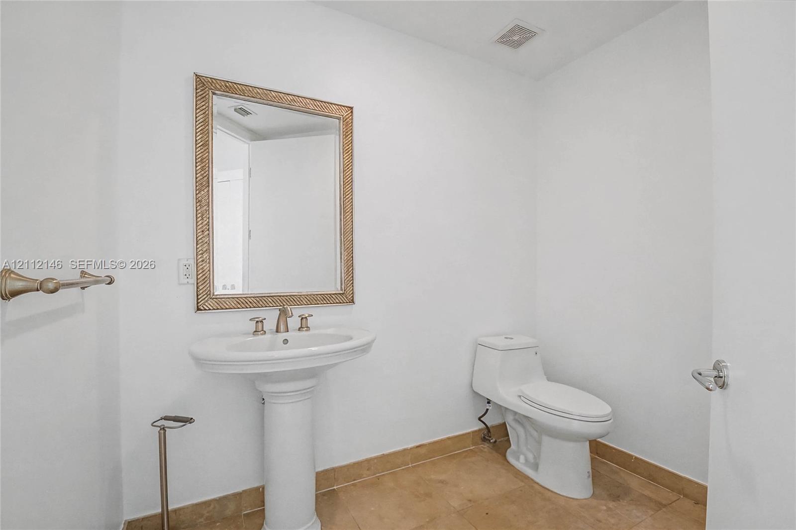 Pedestal sink featuring a metallic faucet, framed wall-mounted mirror, white porcelain toilet, and tile flooring