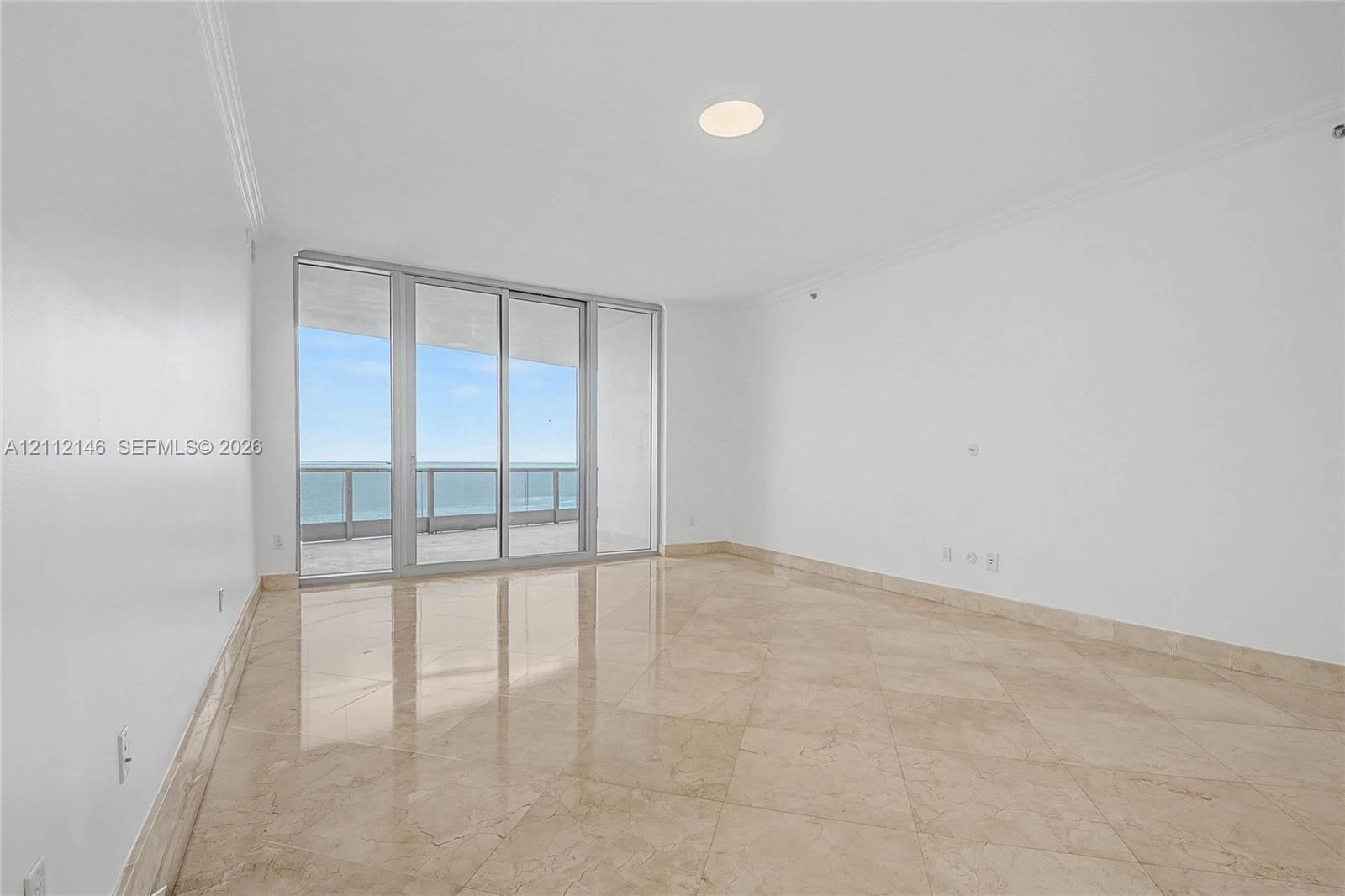 Floor-to-ceiling sliding glass doors, polished stone tile flooring, crown molding, recessed lighting, and a private balcony