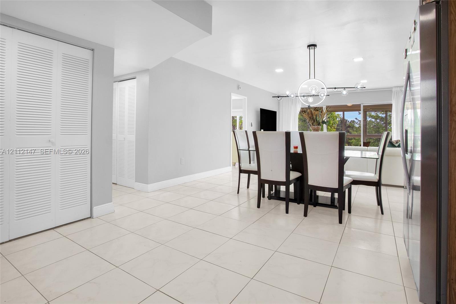 Neutral tile flooring, white louvered-door closets, contemporary circular chandelier, and recessed lighting