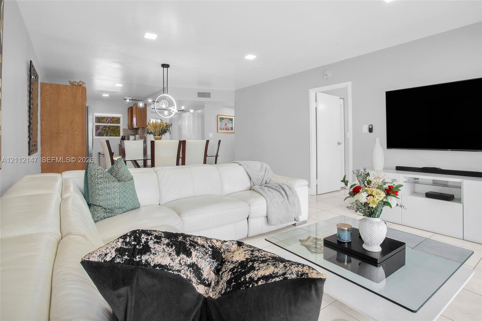 Open-concept interior featuring neutral wall tones, large-format tile flooring, recessed lighting, and a modern circular chandelier fixture