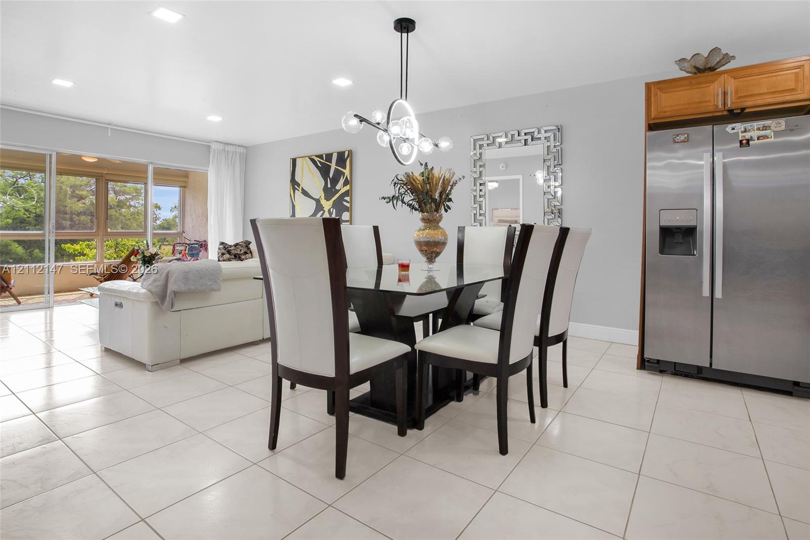 Open-concept area featuring light-toned tile flooring, recessed lighting, a modern multi-light fixture, and large sliding glass doors providing access to the exterior space