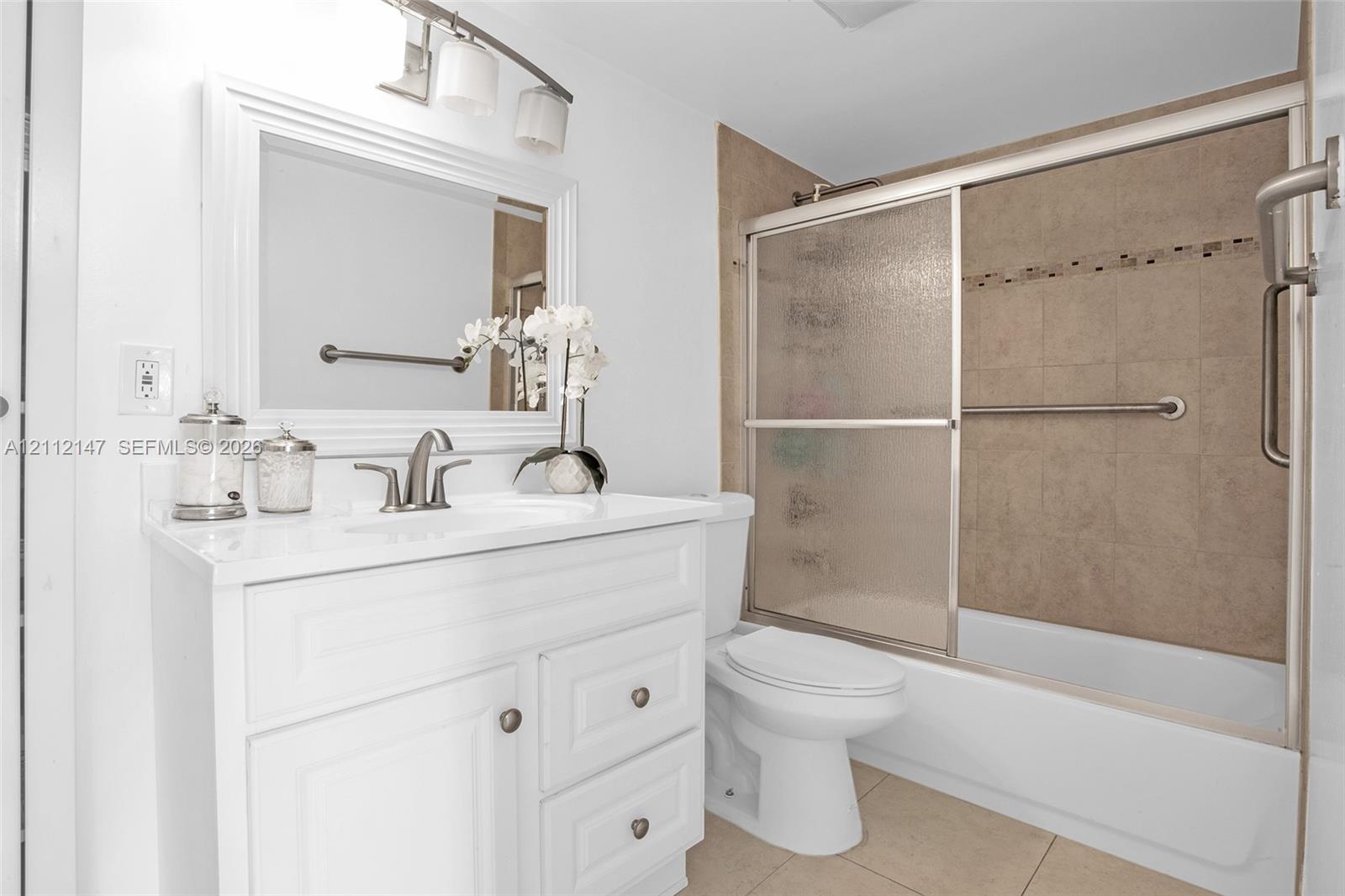 White cabinetry vanity with a countertop basin and multi-light fixture, framed mirror, and a tiled shower-tub combination with sliding glass doors