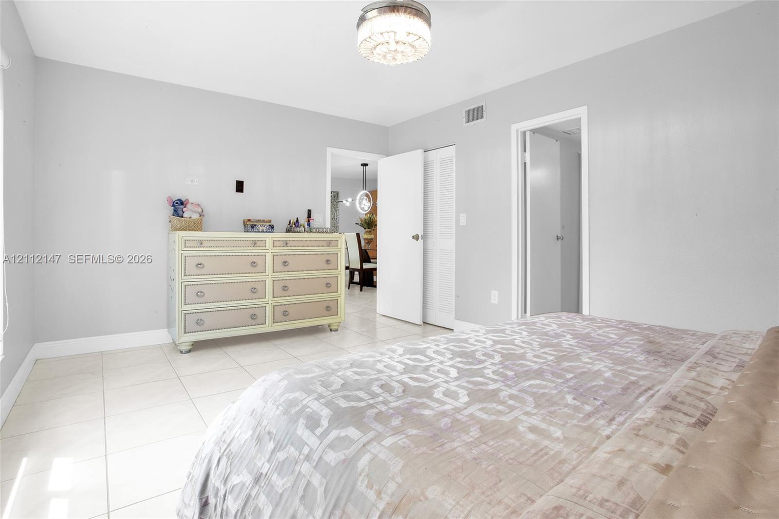 Neutral-toned interior space featuring light-colored tile flooring, flush-mount decorative ceiling light fixture, and louvered-door closet