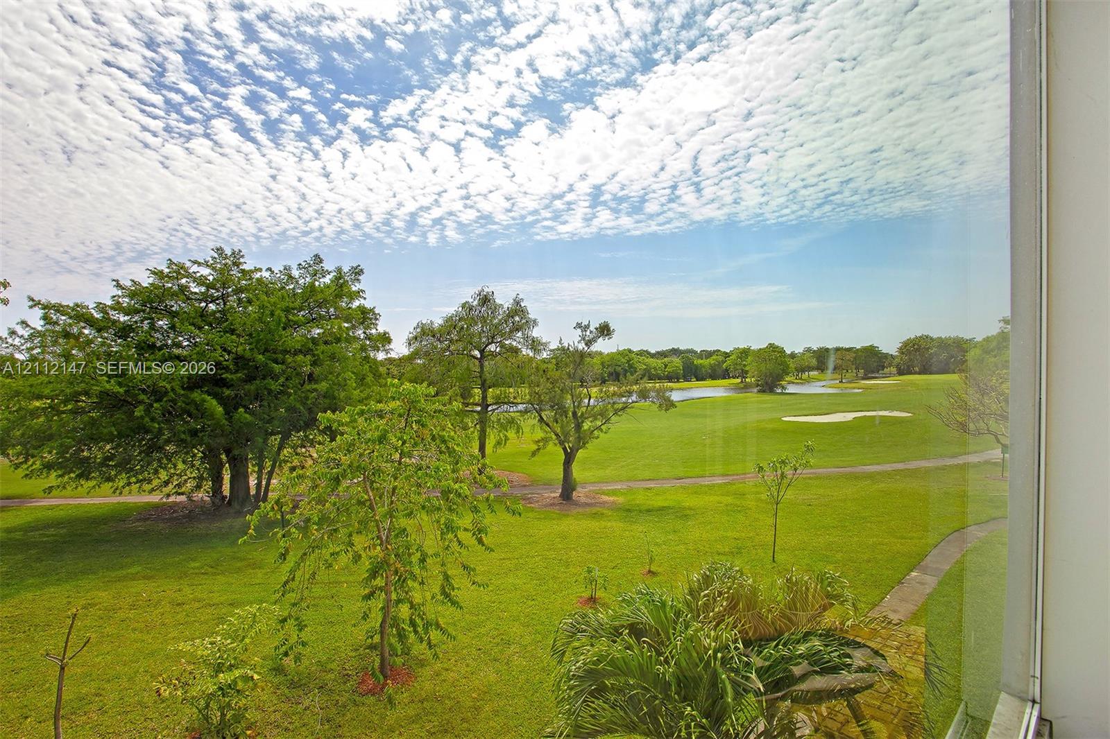 Full-height window pane providing exterior visibility of a landscaped lawn, mature trees, a water feature, and a golf course green