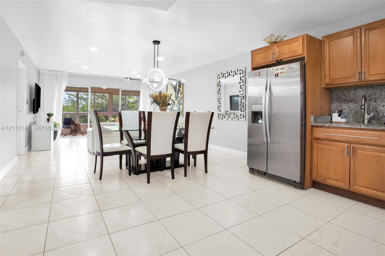 Kitchen area featuring natural wood cabinetry, stone countertops, a stainless steel refrigerator, and large-format tile flooring