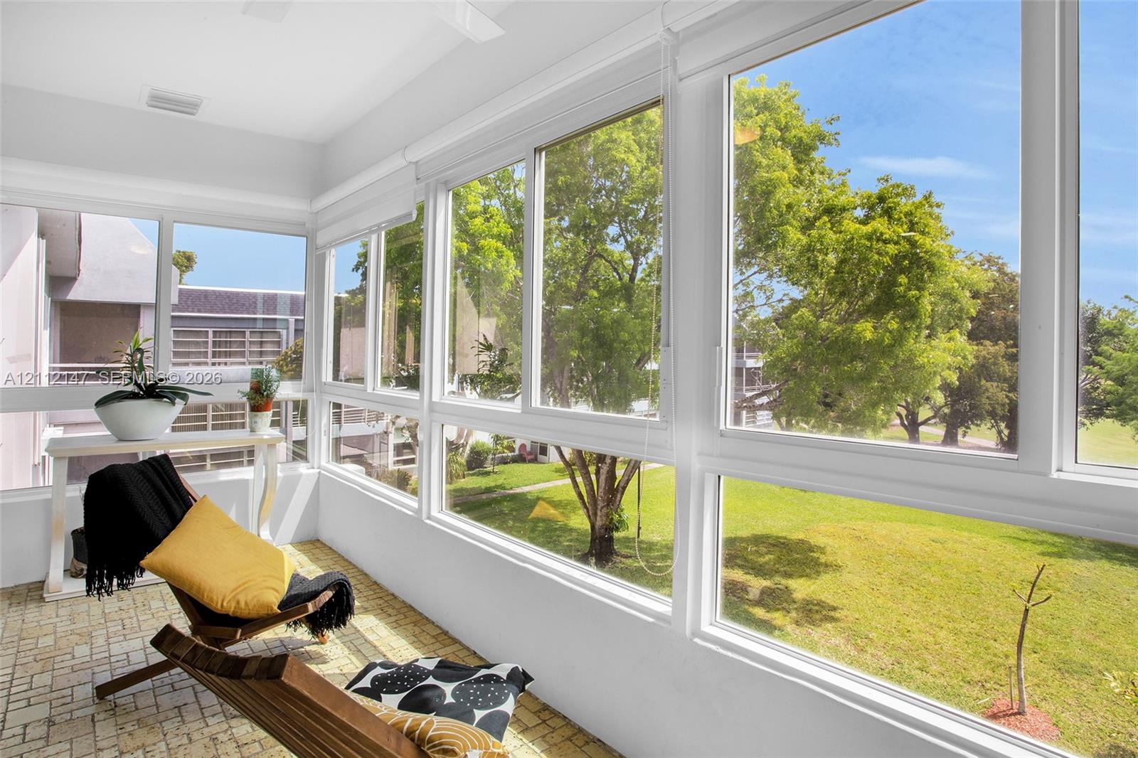 Enclosed sunroom featuring expansive window walls, white-framed glass sliders, and textured stone-finish flooring