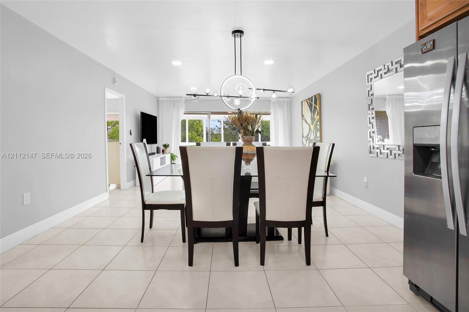 Dining area featuring large-format tile flooring, a geometric multi-light pendant fixture, recessed ceiling lighting, and a stainless steel side-by-side refrigerator