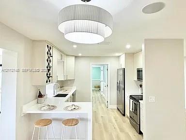 Kitchen featuring tiered pendant lighting, light wood-finish flooring, white cabinetry with built-in wine storage, stone countertops, and stainless steel appliances