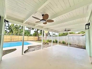 Covered patio featuring a painted wood-beam ceiling, ceiling fans, wall-mounted lanterns, concrete flooring, and an in-ground swimming pool Covered patio featuring a painted wood-beam ceiling, ceiling fans, wall-mounted lanterns, concrete flooring, and an in-ground swimming pool