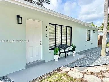 Exterior facade featuring light-toned smooth stucco, a solid entry door with matte black lantern-style sconce, large picture windows with black frames, and a concrete front entry landing