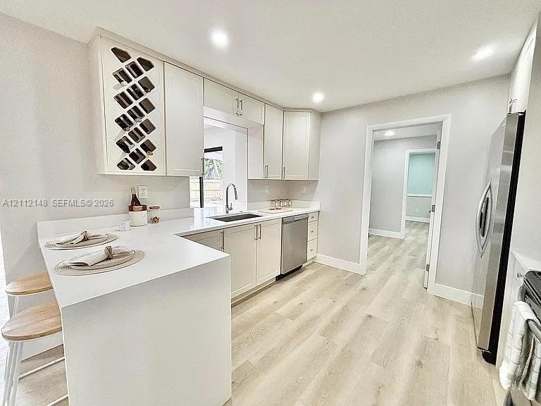 Kitchen featuring white Shaker-style cabinetry with integrated wine rack, solid-surface countertops, stainless steel appliances, and wood-finish flooring