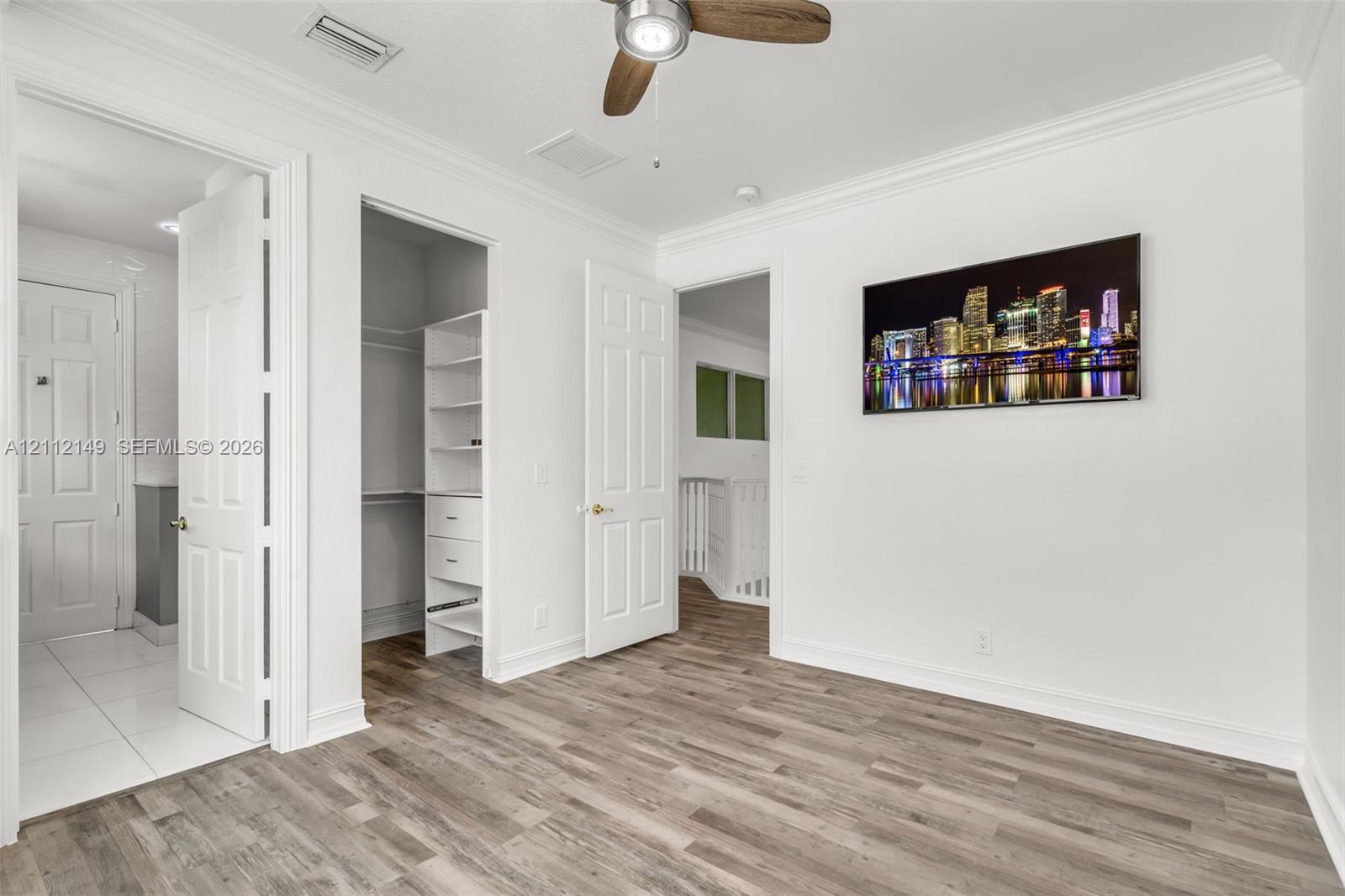 Wood-finish flooring, crown molding, ceiling fan with light kit, and walk-in closet featuring built-in shelving