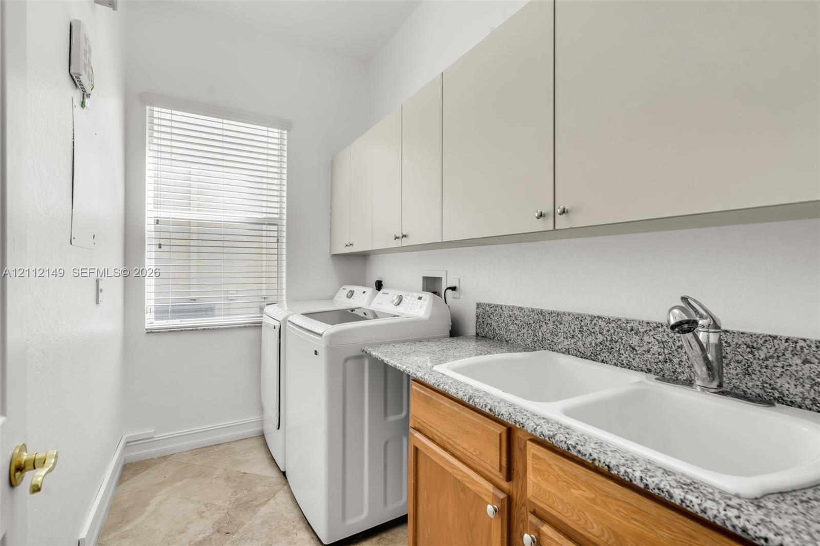 Laundry space featuring stone-composite countertop, dual-basin drop-in sink, chrome pull-down faucet, wooden base cabinetry, and overhead storage cabinets