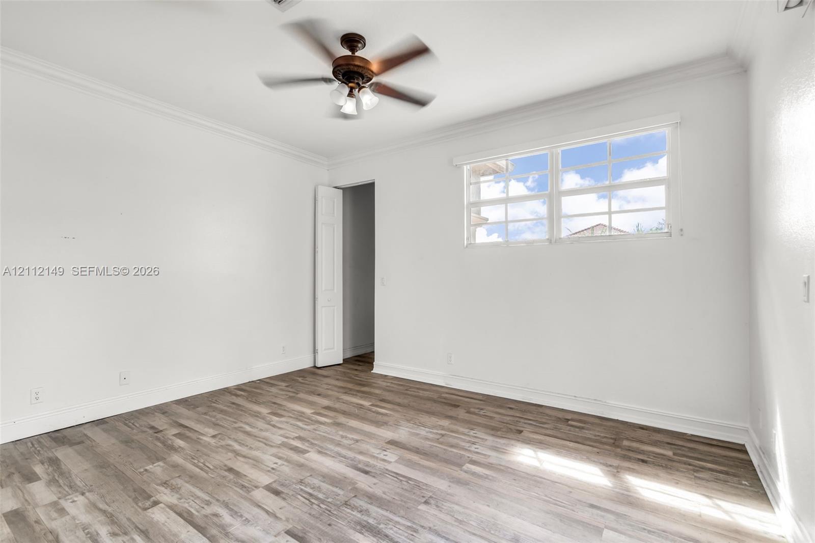Wood-finish flooring, multi-pane window, ceiling fan with integrated lighting, and crown molding