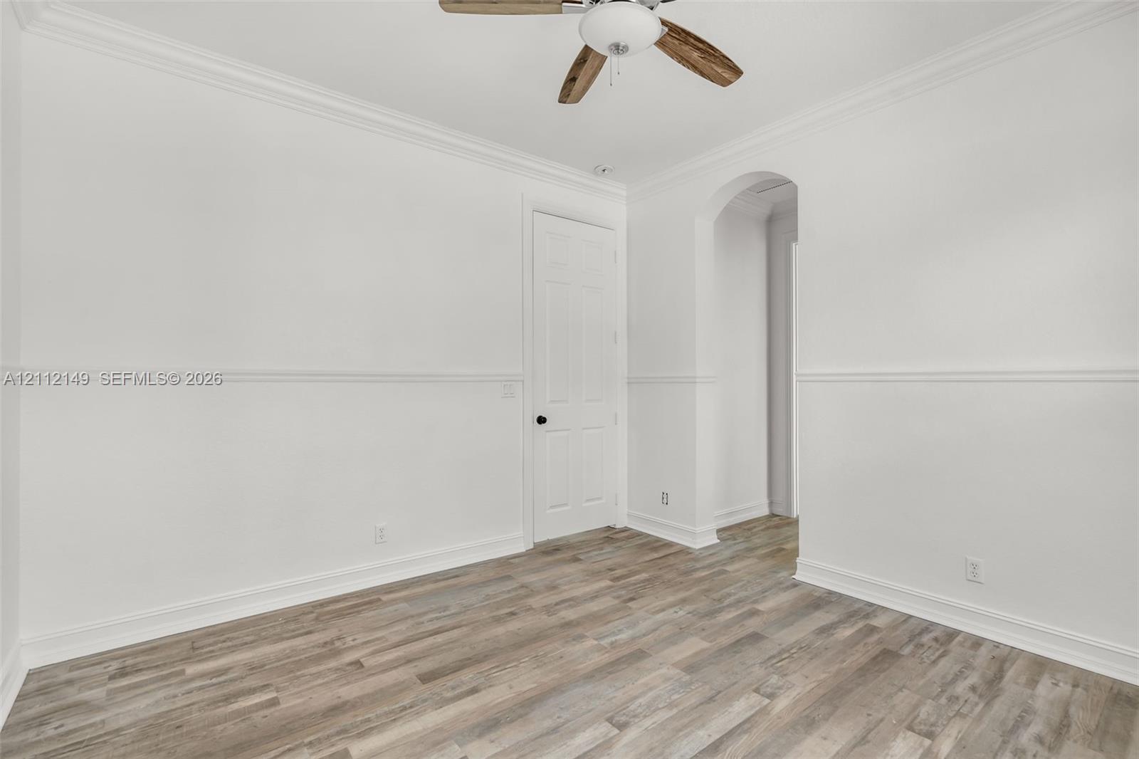 Interior space featuring wood-finish flooring, chair rail molding, crown molding, arched entry, and a ceiling fan with integrated lighting