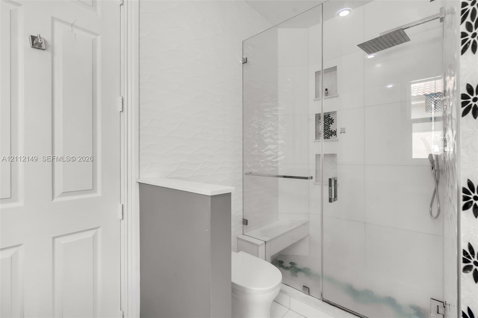 Walk-in shower featuring a glass enclosure, square rainfall shower head, handheld sprayer, built-in bench, and recessed wall niches
