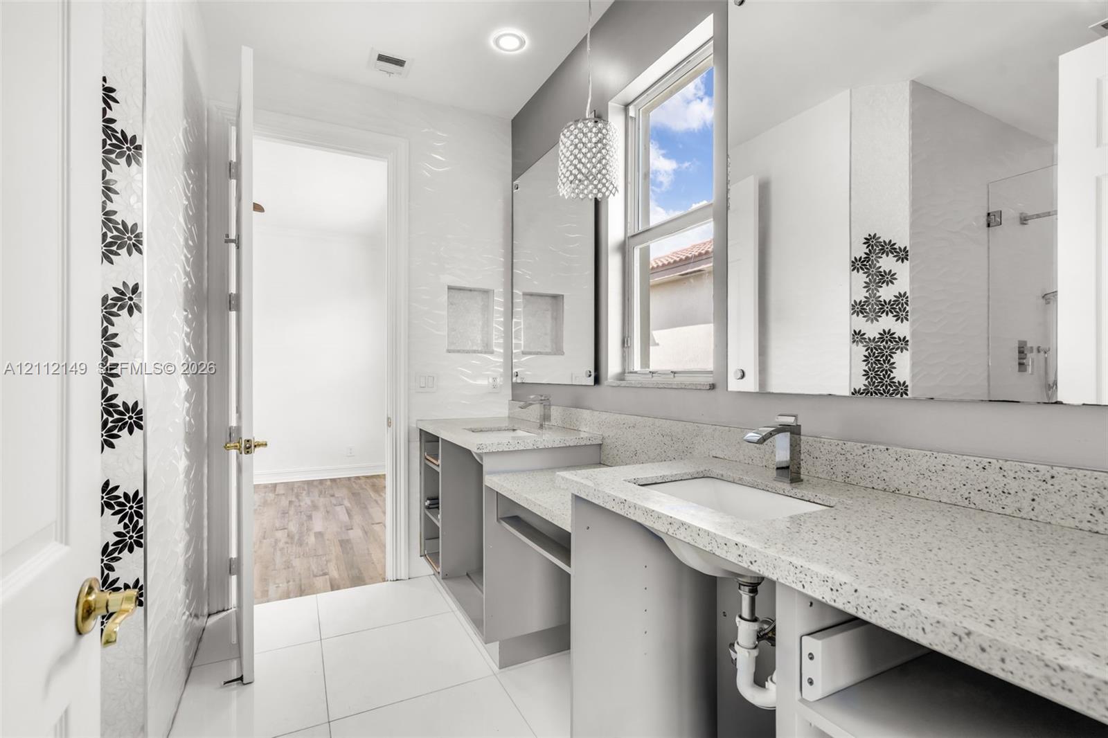 Dual-vanity bathroom featuring speckled stone-finish countertops, undermount sinks, geometric-patterned wall tile accents, and recessed wall shelving