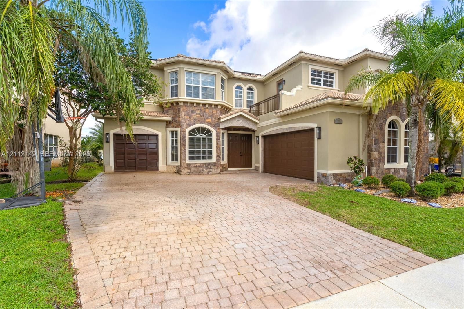 Two-story exterior featuring a stone facade, arched windows, dual garage doors, and a paved driveway