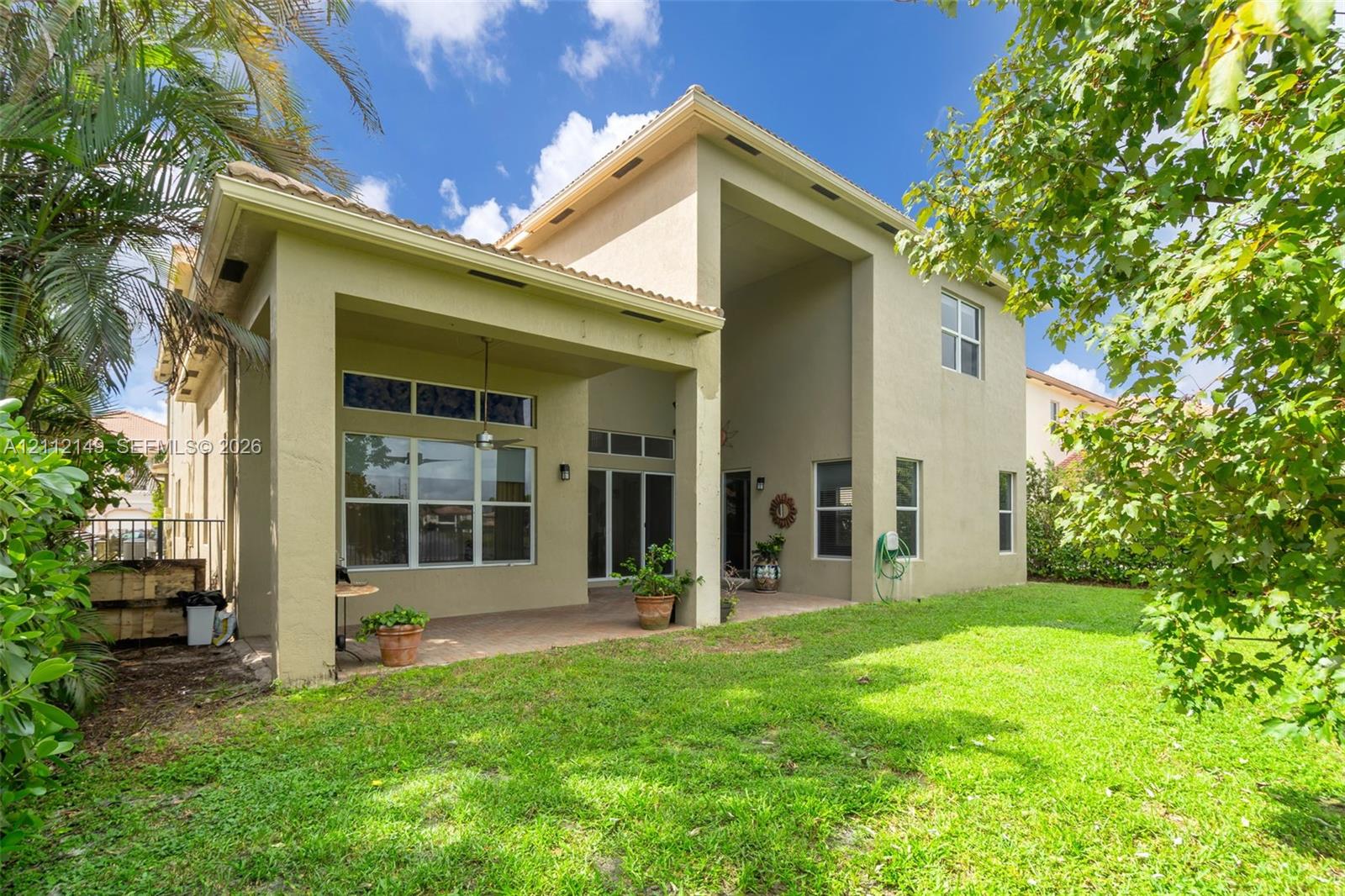 Stucco exterior featuring a covered patio, multi-story architectural design, expansive windows, and a landscaped lawn