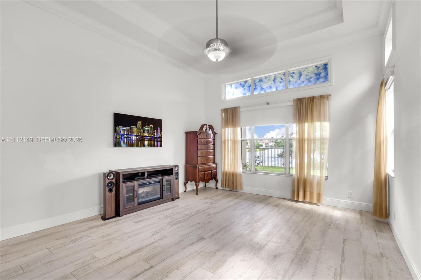 High-ceiling room featuring wood-finish flooring, a tray ceiling with a central ceiling fan, and large windows with a transom above