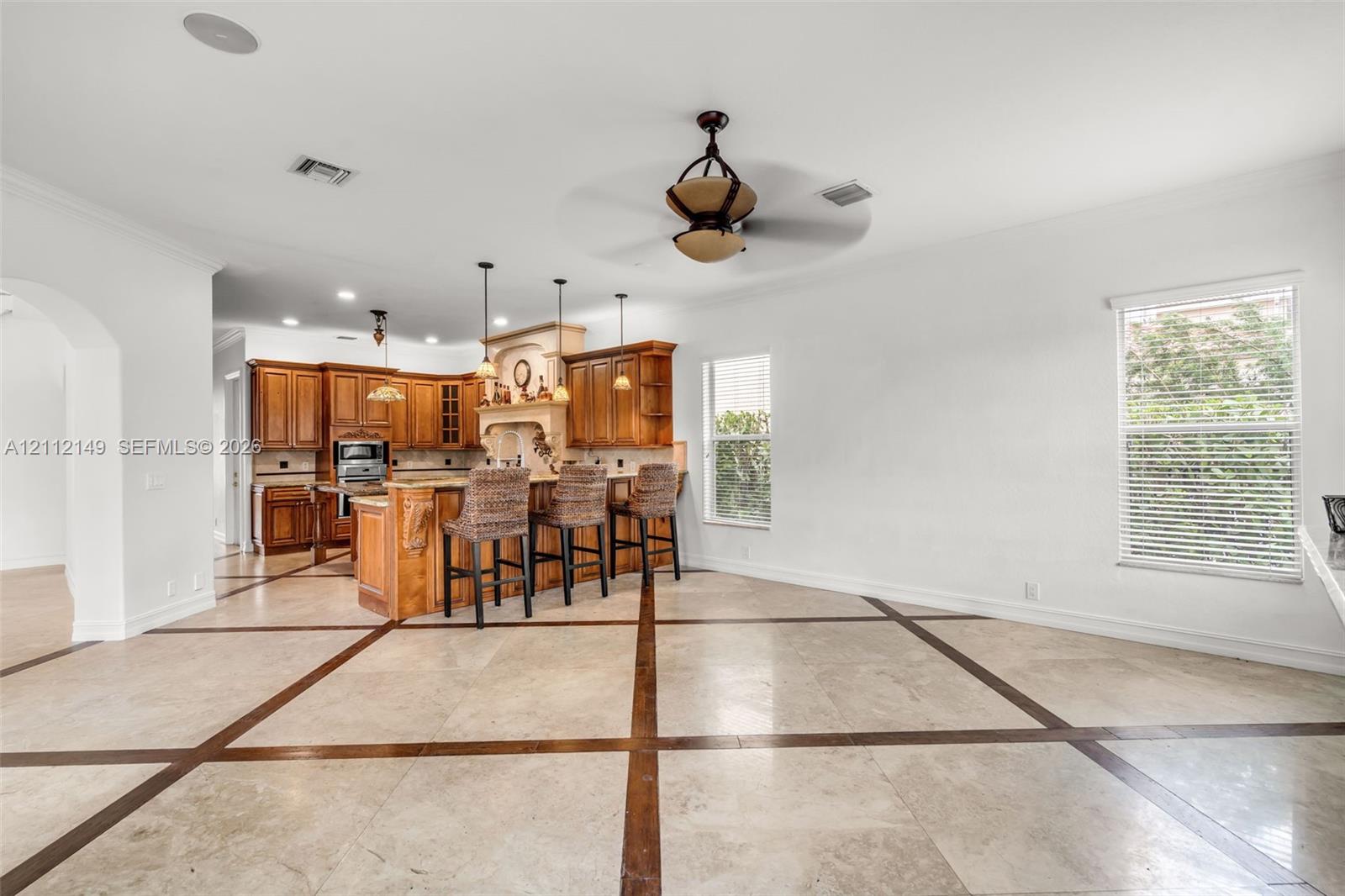 Open-concept kitchen featuring custom wood cabinetry, an expansive center island with pendant lighting, stone flooring with decorative inlay, and recessed lighting