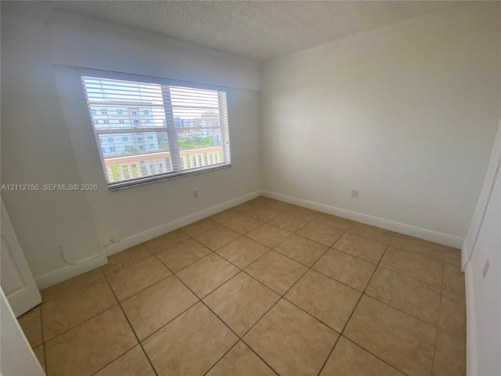 Interior space featuring large-format ceramic tile flooring, neutral walls, and a window with horizontal blinds