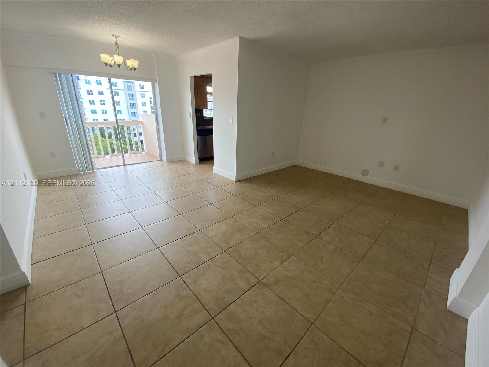 Neutral-toned ceramic tile flooring, sliding glass door with access to a private balcony, and multi-arm chandelier fixture