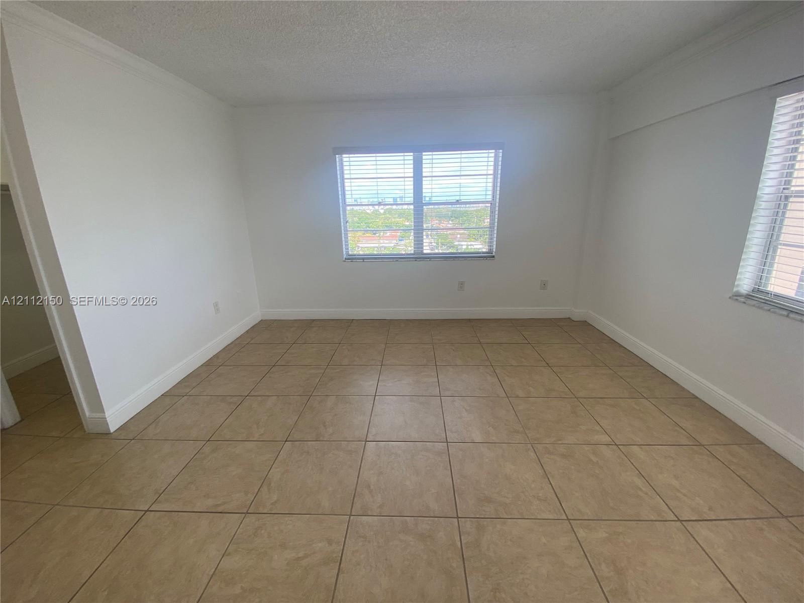 Neutral interior space featuring large-format tile flooring, textured ceilings, dual windows with horizontal blinds, and a built-in walk-in closet