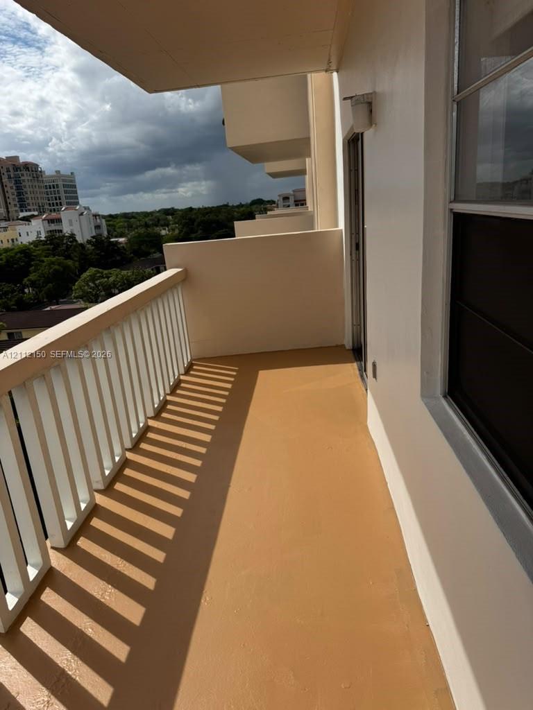 Private balcony featuring a painted concrete floor, vertical spindle railing, and a wall-mounted exterior light fixture