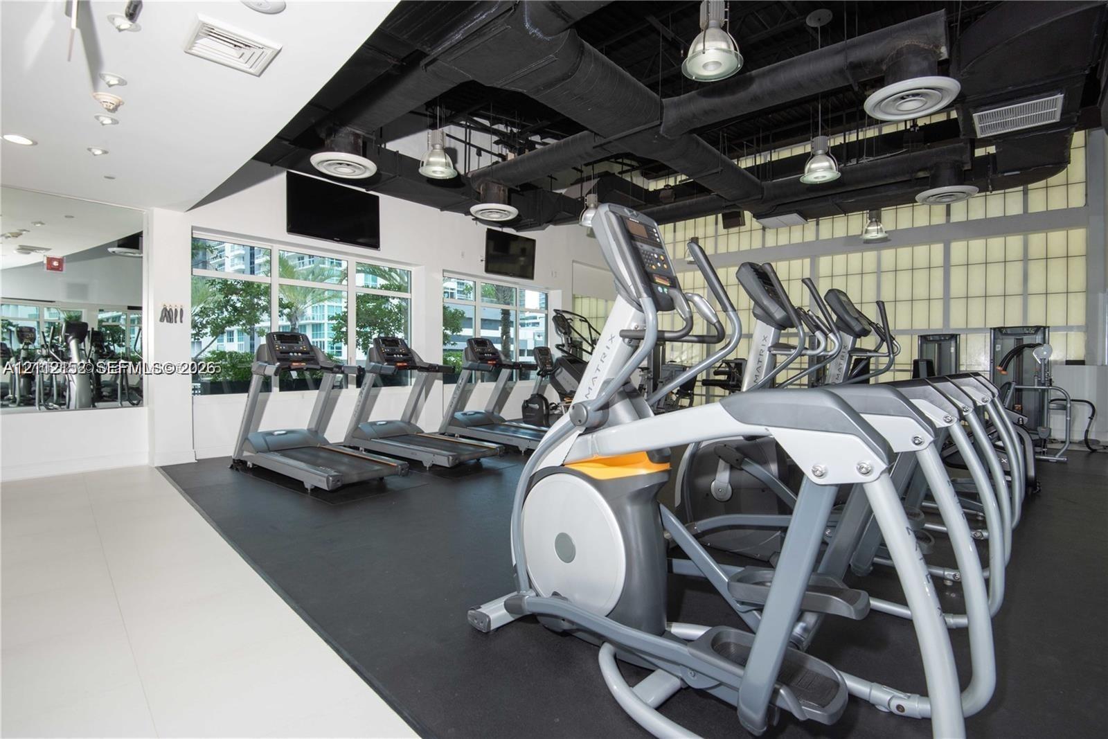 Fitness center featuring large-format windows, industrial-style exposed ceiling, recessed lighting, rubber flooring, and full-wall mirrors