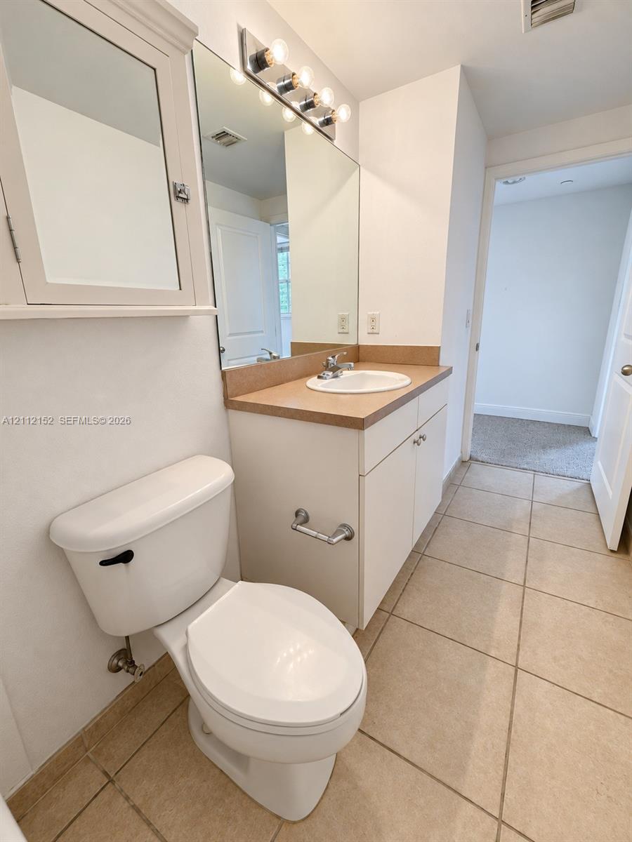 Bathroom featuring ceramic tile flooring, a white vanity cabinet with a solid-surface countertop, an oval drop-in sink, and a wall-mounted medicine cabinet