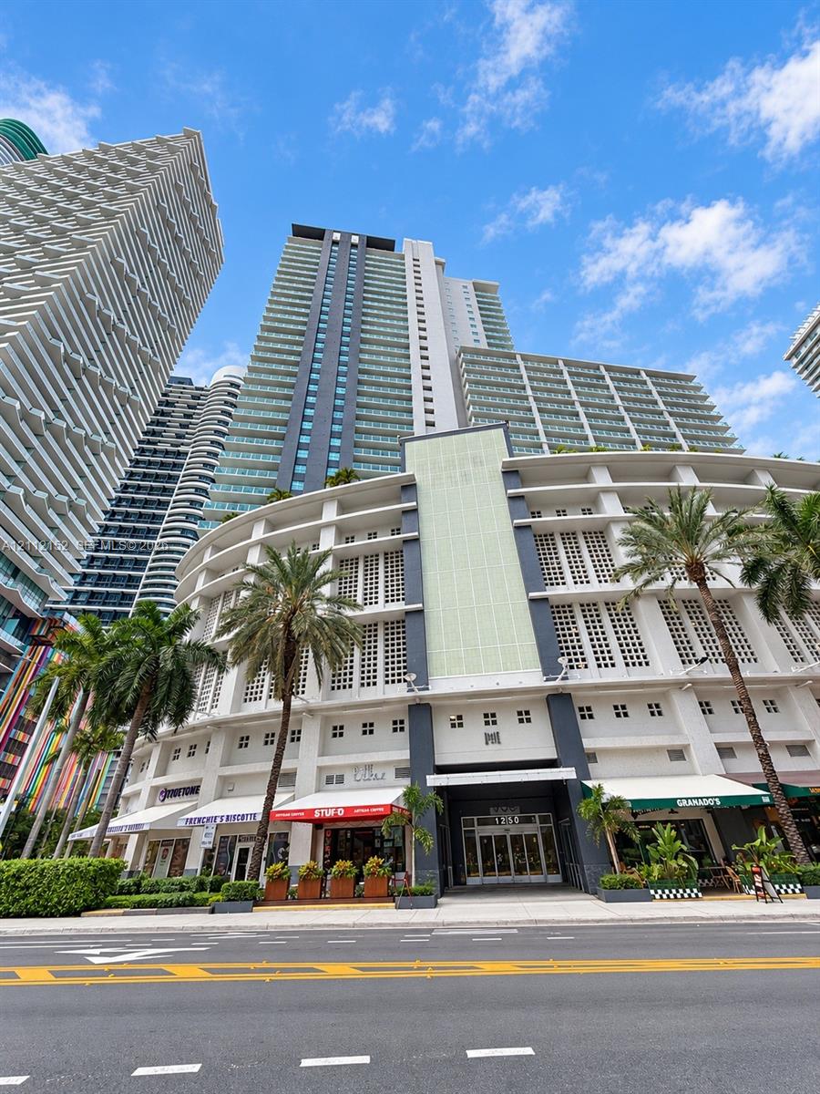 High-rise tower featuring glass-paneled balconies, a multi-level structured facade with architectural detailing, and street-level commercial storefronts