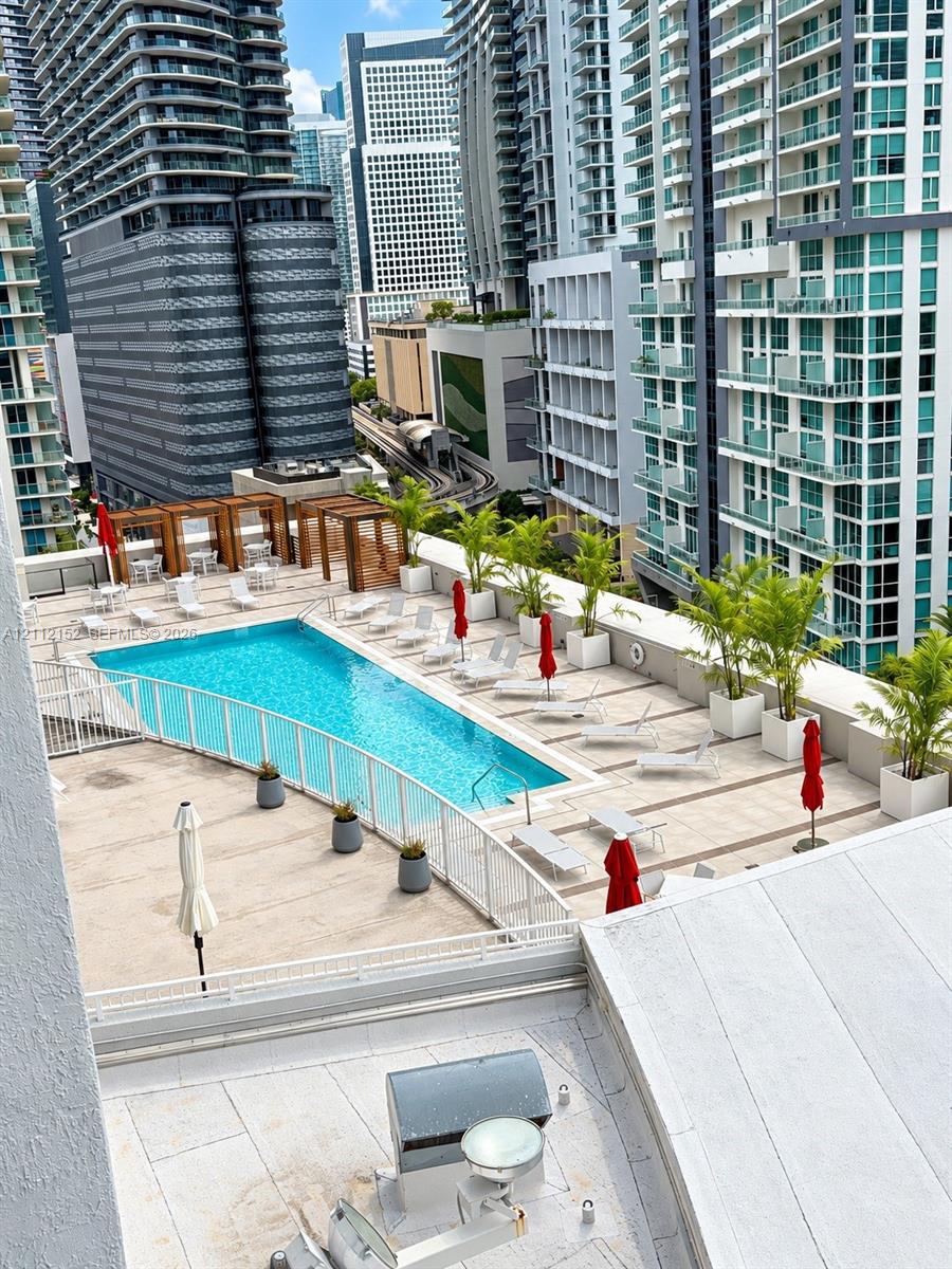 Rooftop pool deck featuring concrete tile surfacing, glass safety railings, wood-slat pergolas, and potted palm landscaping