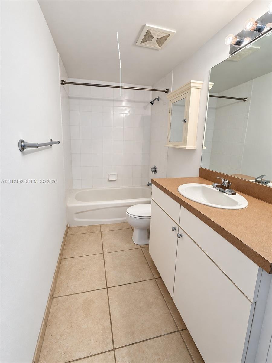 Bathroom featuring a white vanity cabinet with a solid surface countertop, an oval undermount sink, tiled flooring, and a shower-tub combination with white wall tile