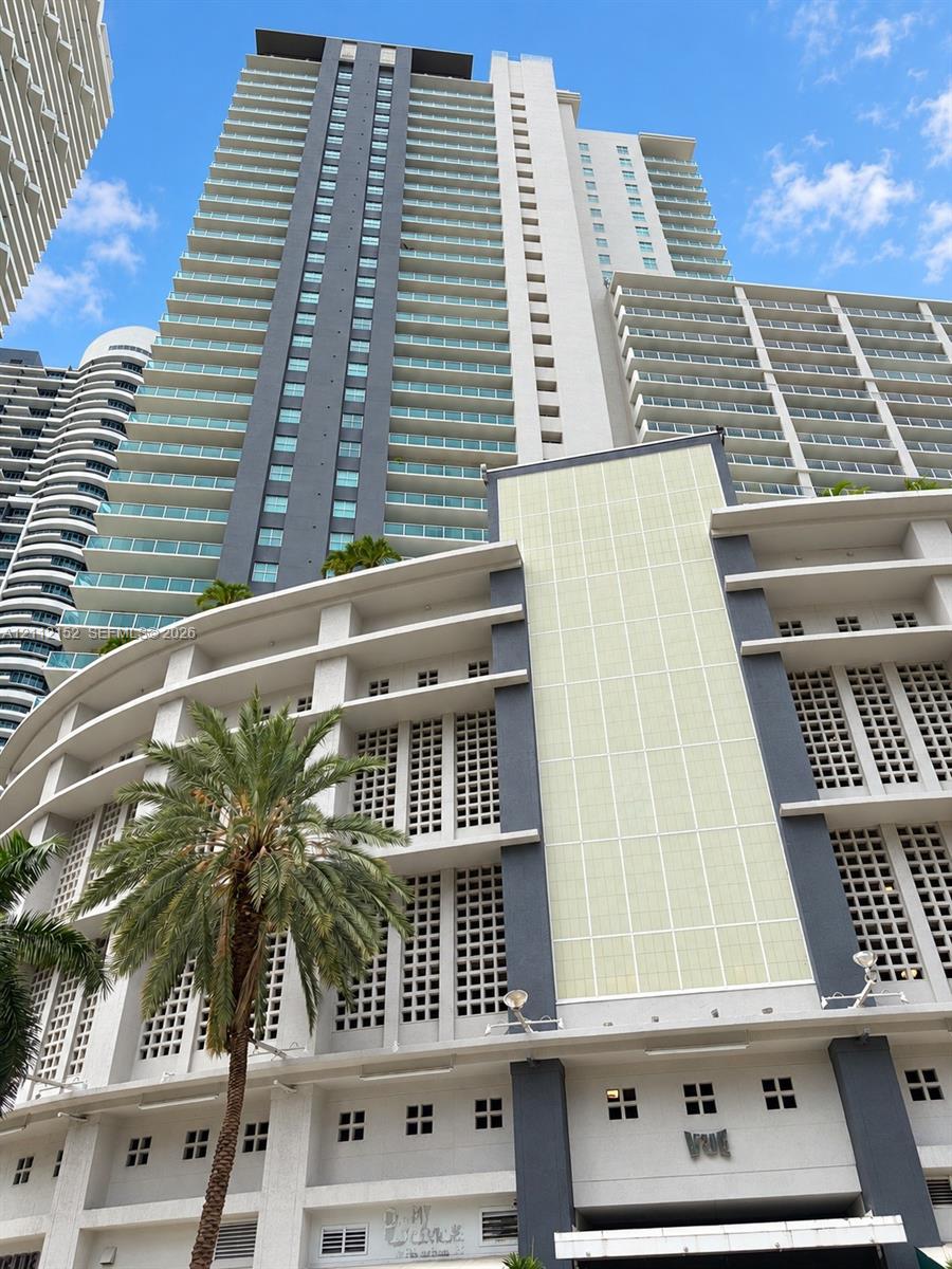 High-rise architectural exterior featuring tiered balconies with glass railings, concrete facade with grid-patterned screening, and vertical dark-tone accent panels