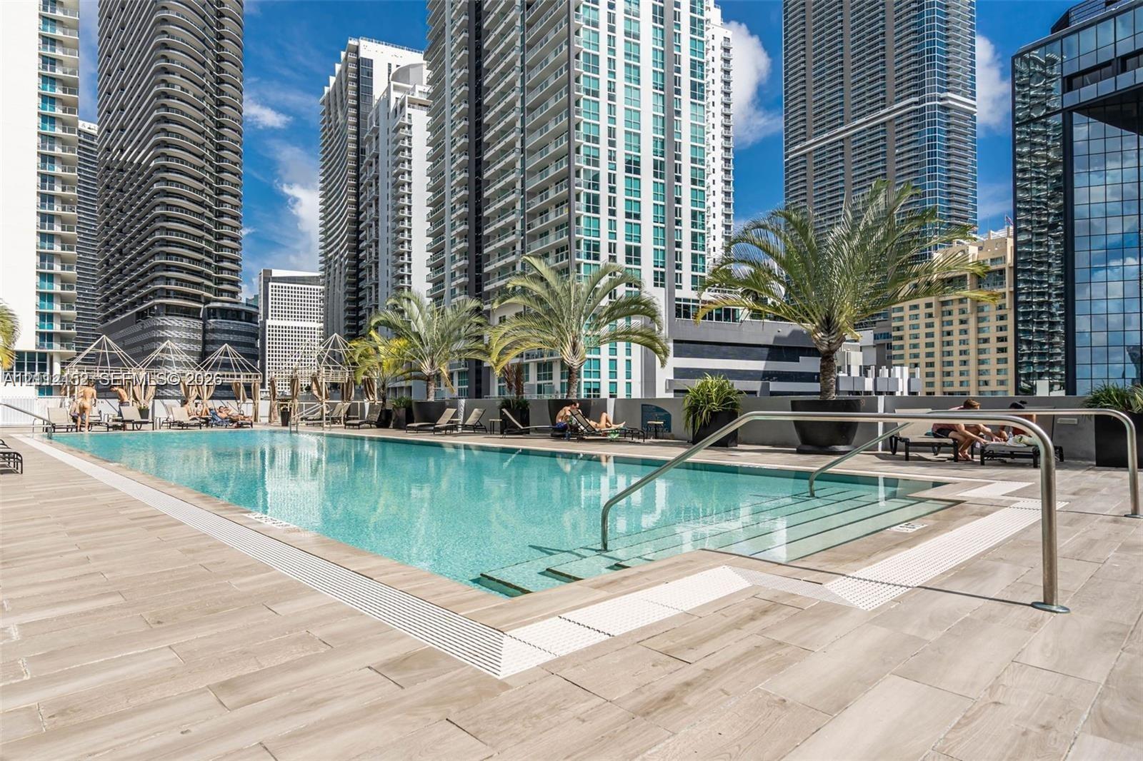 Swimming pool featuring wood-finish tile decking, metal handrails, integrated stair entry, and large-scale decorative planters