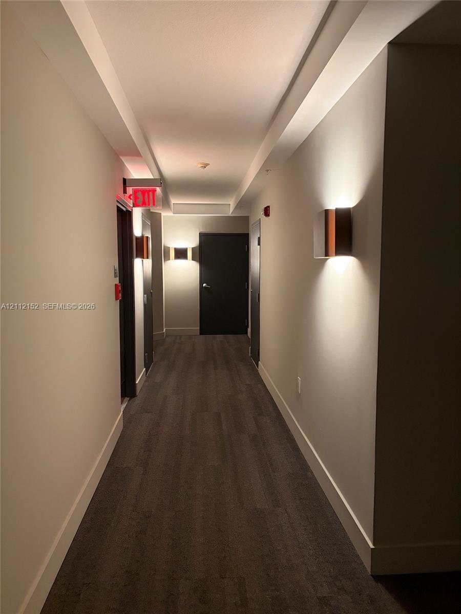 Hallway featuring wood-finish flooring, recessed ceiling lighting, and wall-mounted sconces