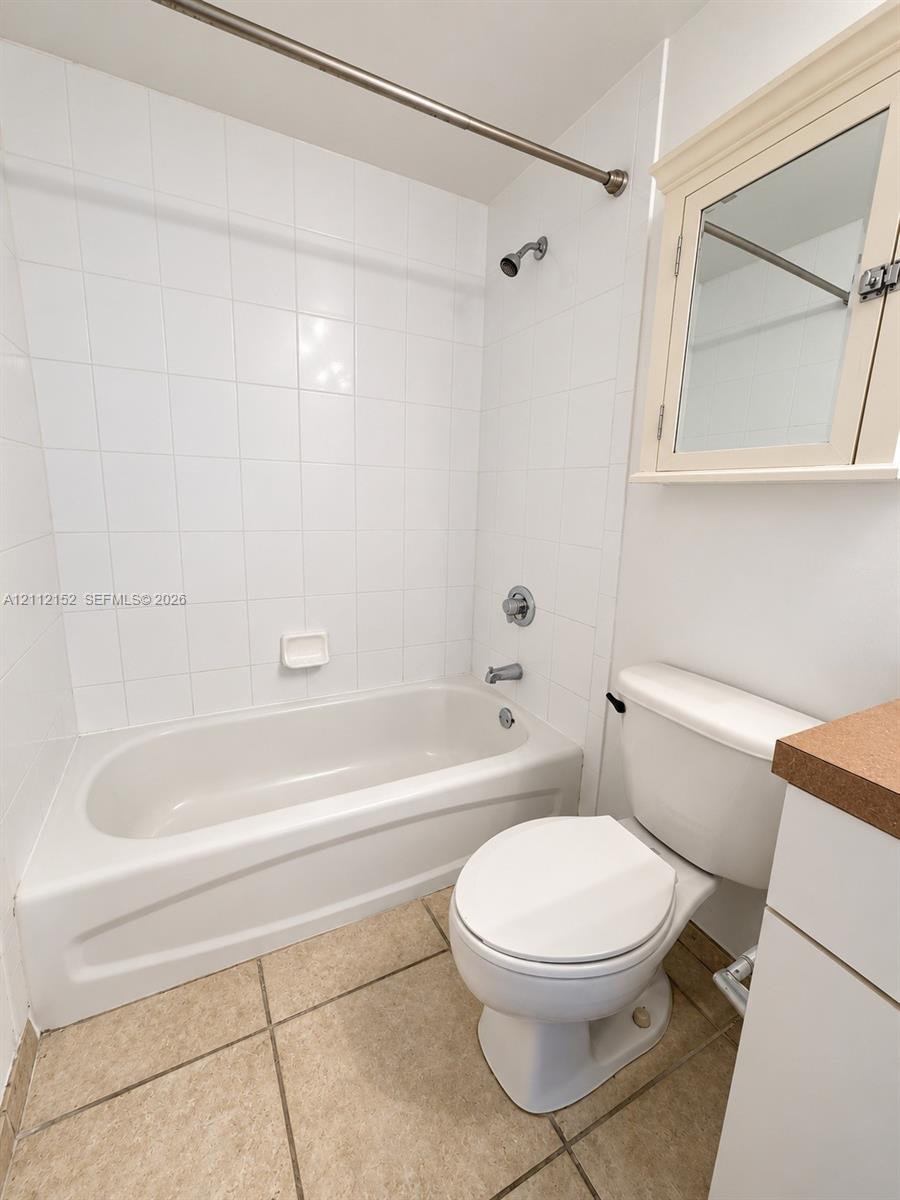 Bathroom featuring tile flooring, a tub-shower combination with full-height wall tiling, built-in medicine cabinet, and a solid-surface vanity countertop