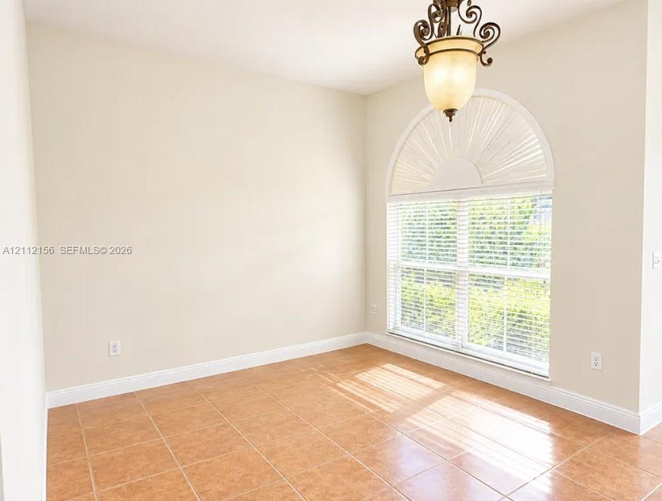 Arched window with decorative fanlight, neutral wall tones, large-format tile flooring, and decorative multi-arm pendant lighting