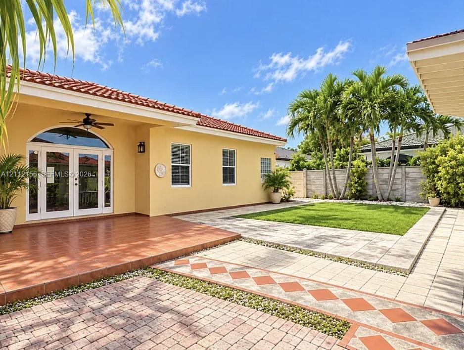 Backyard featuring a covered terrace with ceramic tile flooring, a paver patio with a geometric inlay design, a manicured lawn, and a privacy wall