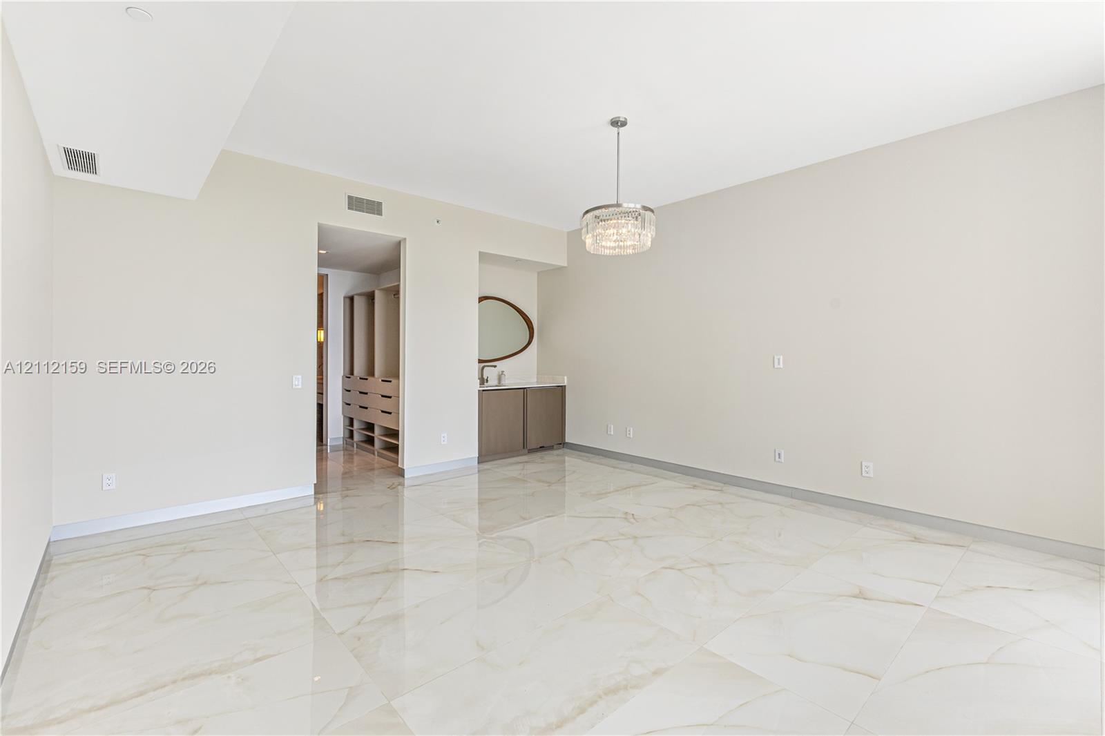 Expansive room featuring polished stone flooring, built-in cabinetry with a stone countertop, custom walk-in closet shelving, and a modern drum pendant light