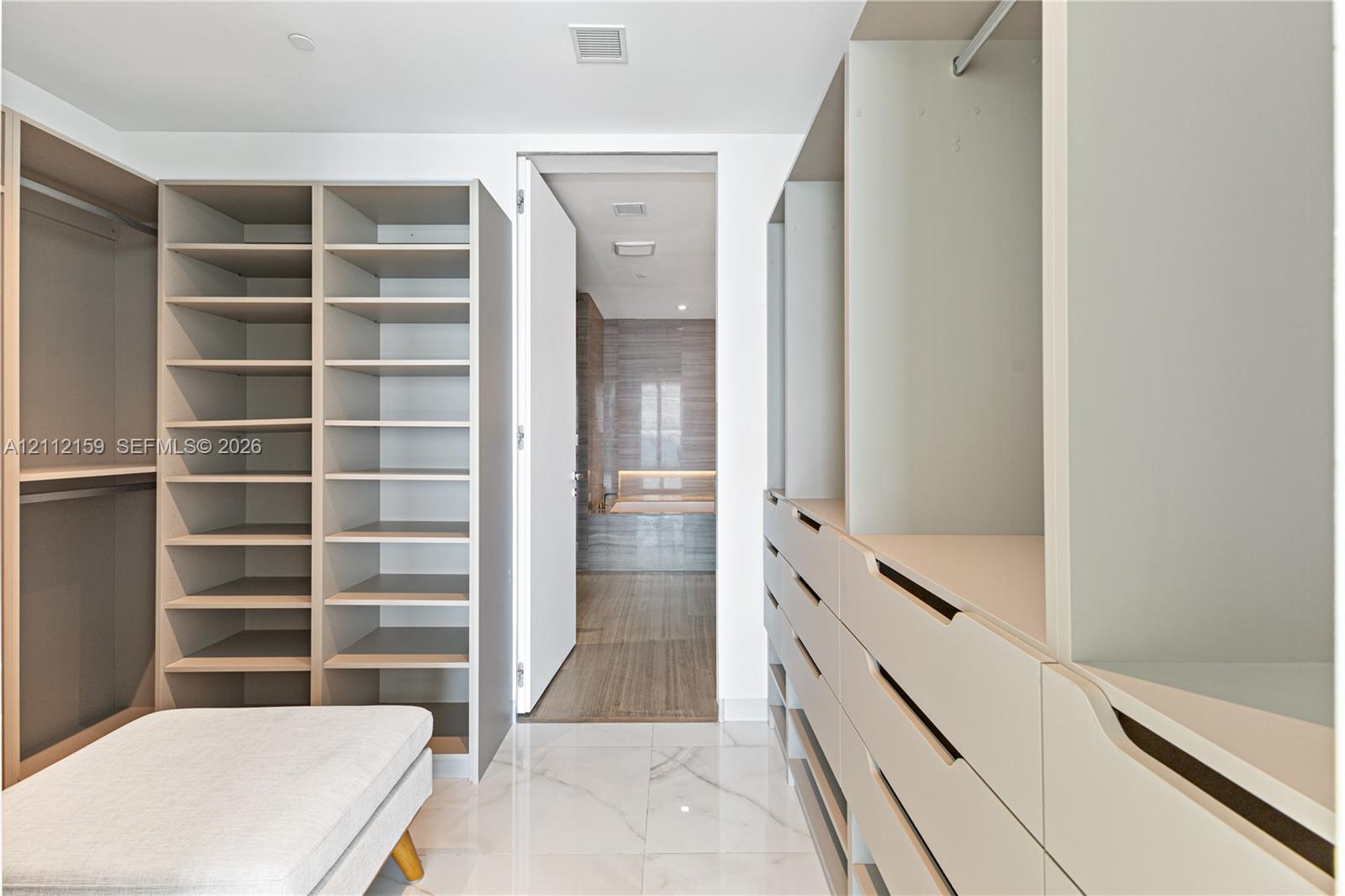 Walk-in closet featuring extensive built-in cabinetry, floor-to-ceiling shelving, recessed drawer units, and polished stone-finish flooring