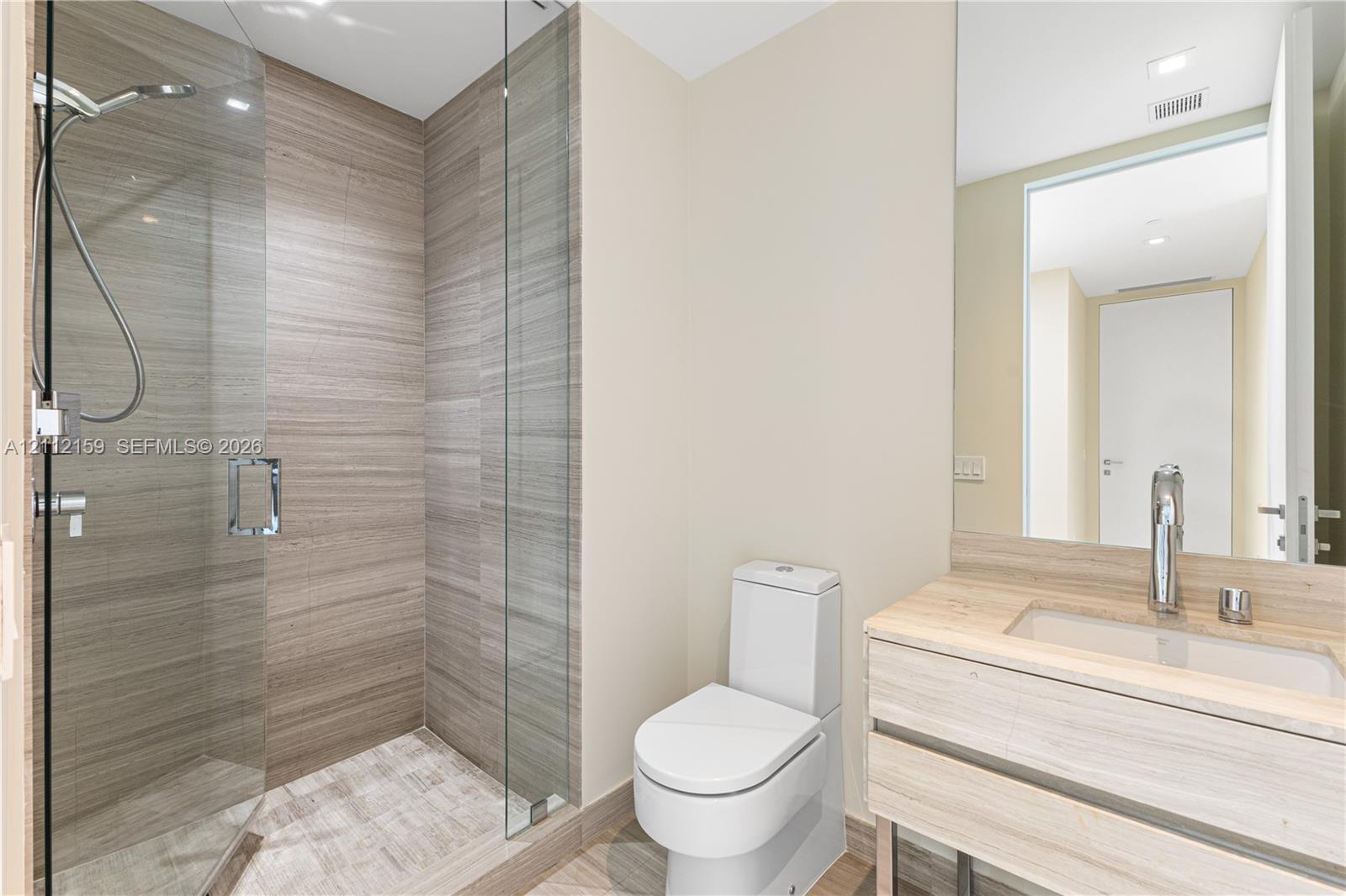 Walk-in shower with wood-finish tile surround and glass enclosure, floating vanity with integrated rectangular sink, wall-mounted faucet, and flush-mount lighting